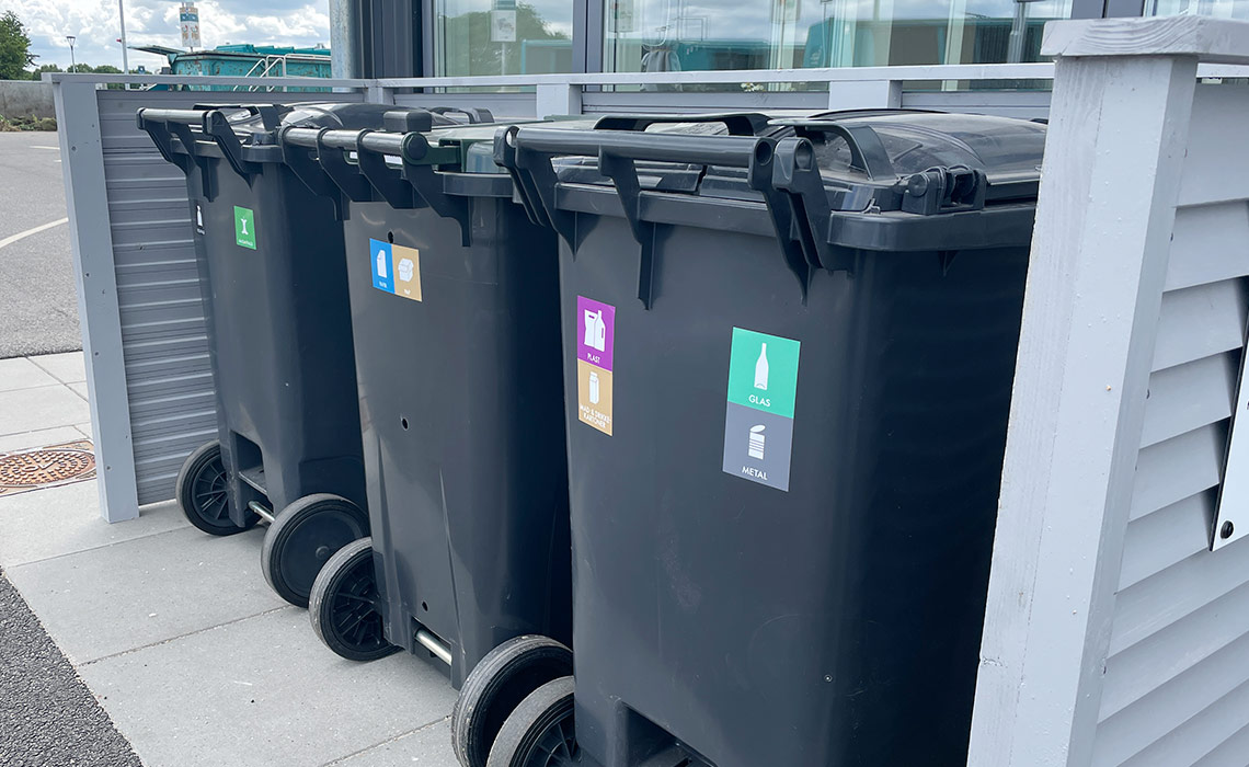 Tre affaldsbeholdere med piktogrammer i skjul på genbrugsplads